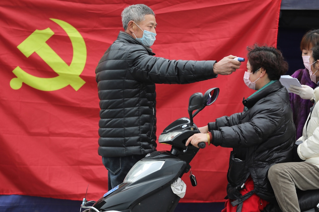 (Chinatopix via AP) A volunteer stands in front of a Communist Party flag as he takes the temperature of a scooter driver at a roadside checkpoint in Hangzhou in eastern China's Zhejiang Province, Monday, Feb. 3, 2020. China sent medical workers and equipment to a newly built hospital, infused cash into financial markets and further restricted people's movement in sweeping new steps Monday to contain a rapidly spreading virus and its escalating impact.