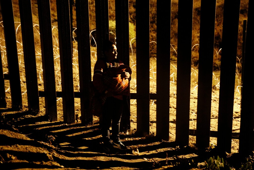 A woman holding a baby peers through the U.S. border fence as she tries to reach a point where scores of migrants have been crossing in recent days, now blocked by private security, in Playas de Tijuana, Mexico, Wednesday, Dec. 5, 2018. Legal groups argue that federal law states that immigrants can apply for asylum no matter how they enter U.S. territory. (AP Photo/Rebecca Blackwell)
