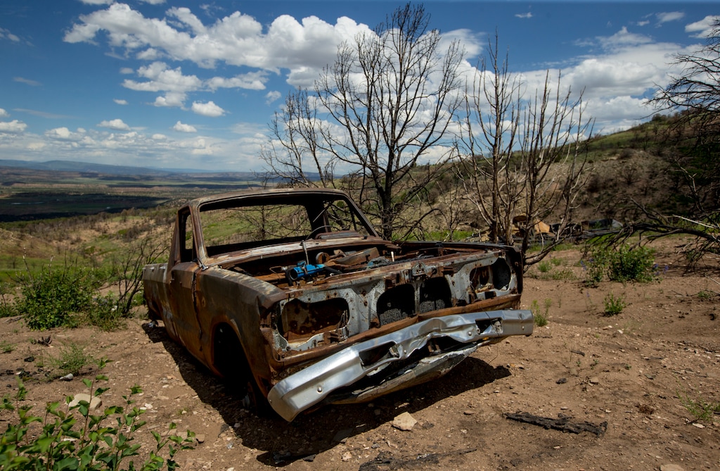 (Isaac Hale/The Daily Herald via AP) In this Monday, July 8, 2019 photo, a burned pickup truck remains beside where a mobile home once stood during a tour to examine conditions near the Wildcat Wildlife Management Area roughly a year after a wildfire in Duchesne County, Utah. The Daily Herald reports that grasses and flowers are returning to the area alongside charred trees. Other vegetation, like trees and sagebrush, are expected to take longer.
