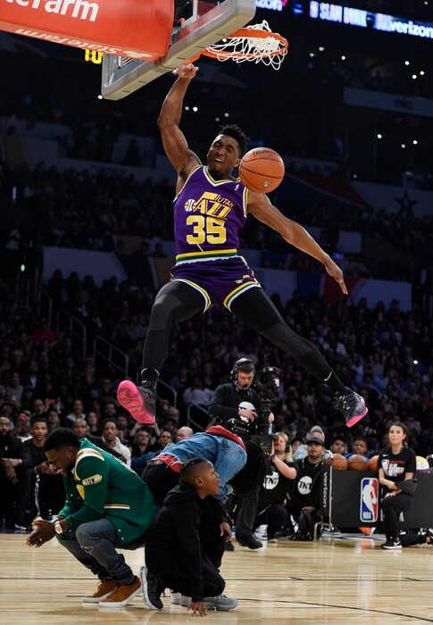 Utah Jazz's Donovan Mitchell, top, dunks over three people, including actor Kevin Hart, left, during the NBA All-Star basketball Slam Dunk contest, Saturday, Feb. 17, 2018, in Los Angeles. (AP Photo/Chris Pizzello)