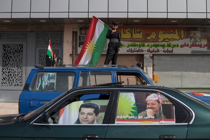 A boy carries a Kurdish flag on top of a car as a car with the faces of Kurdish president Masoud Barzani and his son Masrour on the windows passes by in the disputed city of Kirkuk, Monday, Sept. 25, 2017. Iraq's Kurdish region vote in a referendum on whether to secede from Iraq. (AP Photo/Bram Janssen)