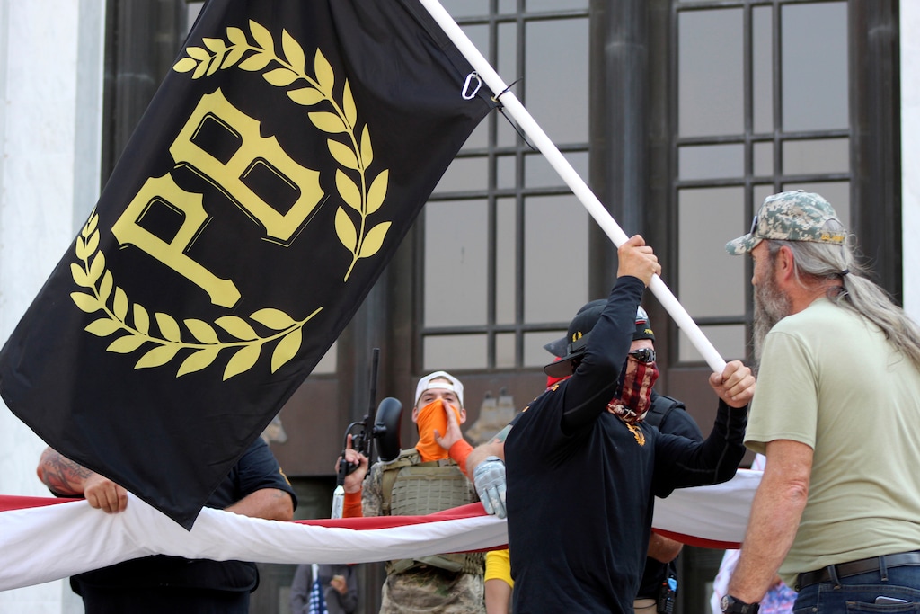 (Andrew Selsky | AP file photo)
In this Sept. 7 photo, a protester carries a Proud Boys banner, symbol of a right-wing group, while other members start to unfurl a large U.S. flag in front of the Oregon State Capitol in Salem, Ore. President Donald Trump didn't condemn white supremacist groups and their role in violence in some American cities this summer. Instead, he said the violence is a “left-wing" problem and he told one far-right extremist group to “stand back and stand by.” His comments Tuesday night were in response to debate moderator Chris Wallace asking if he would condemn white supremacists and militia groups. Trump's exchange with Democrat Joe Biden left the extremist group Proud Boys celebrating what some of its members saw as tacit approval.