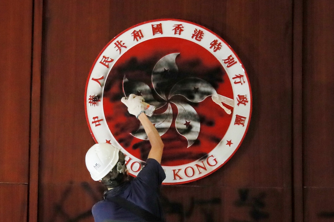 (Kin Cheung | AP Photo) A protester defaces the Hong Kong emblem after they broke into the Legislative Council building in Hong Kong, Monday, July 1, 2019. Protesters in Hong Kong took over the legislature's main building Monday night, tearing down portraits of legislative leaders and spray painting pro-democracy slogans on the walls of the main chamber.