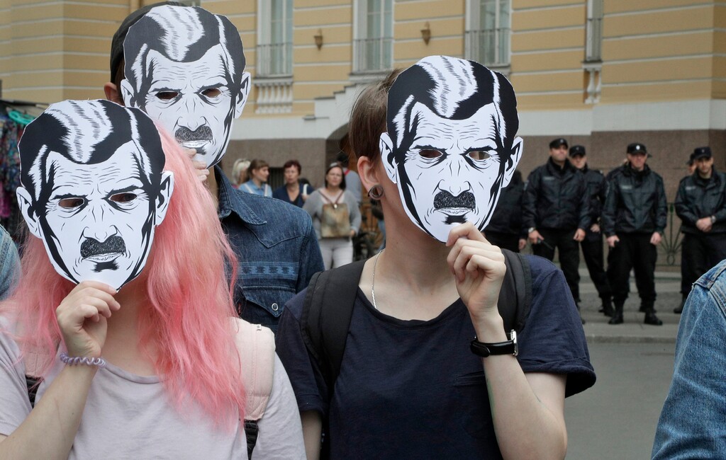 Watched by police people wear face masks depicting the Big Brother character from George Orwell's novel Nineteen Eighty-Four, as they attend a protest rally 'For freedom on the Internet', in St.Petersburg, Russia, Sunday, July 16, 2017. About 30 activists gathered in central St.Petersburg to protest against the thoughtcrime censorship by the state on the Internet in Russia. (AP Photo/Dmitri Lovetsky)