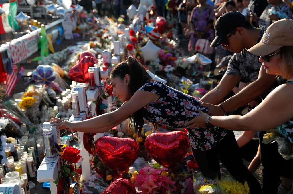 A woman leans over to write a message on a cross at a makeshift memorial at the scene of a mass shooting at a shopping complex, Tuesday, Aug. 6, 2019, in El Paso, Texas. (AP Photo/John Locher)