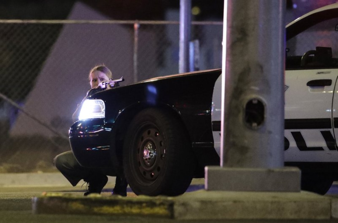 A Las Vegas police officer takes cover at the scene of a mass shooting that left at least 50 people dead and hundreds more hurt. (AP Photo)