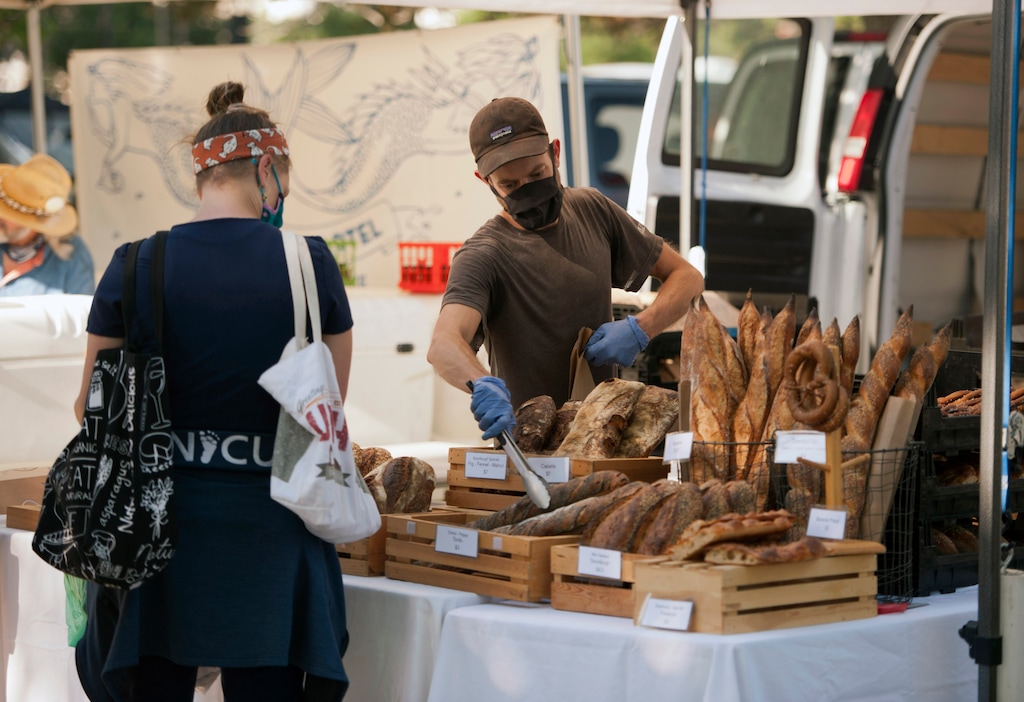 (Ed Kosmicki | Special to the Tribune) The Downtown Farmers Market was back in nearly full swing  Saturday June 5, 2021 at Pioneer Park for the first time since COVID19 pandemic started in March, 2019. Bread Riot owner Phillip Massey bags a baggette for Julianna Webster. The Bread Riot tent had the longest lines at the opening day of the 2021 Summer Farmers Market and sold out its inventory in about 3 hours.