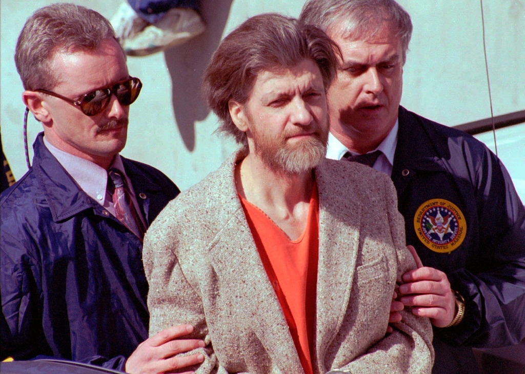 (John Youngbear | The Associated Press) In this April 4, 1996 file photo Theodore John Kaczynski is flanked by federal agents as he is led to a car from the federal courthouse in Helena, Mont. A federal grand jury in San Francisco indicted Vladislav Victorvic Timoshchuk, on charges of mailing two envelopes containing ricin to Pelican Bay State Prison, officials announced on Friday Feb. 21, 2020. Last year the federal Bureau of Prisons intercepted a Christmas card from Timoshchuk, now living in Belarus, to Kaczynski, the convicted Unabomber, which authorizes say Timoshchuk discussed his plan to mail ricin to the United States. Kaczynski is serving a life sentence in a federal prison in Colorado for carrying out a series of mail bombings that killed three people.