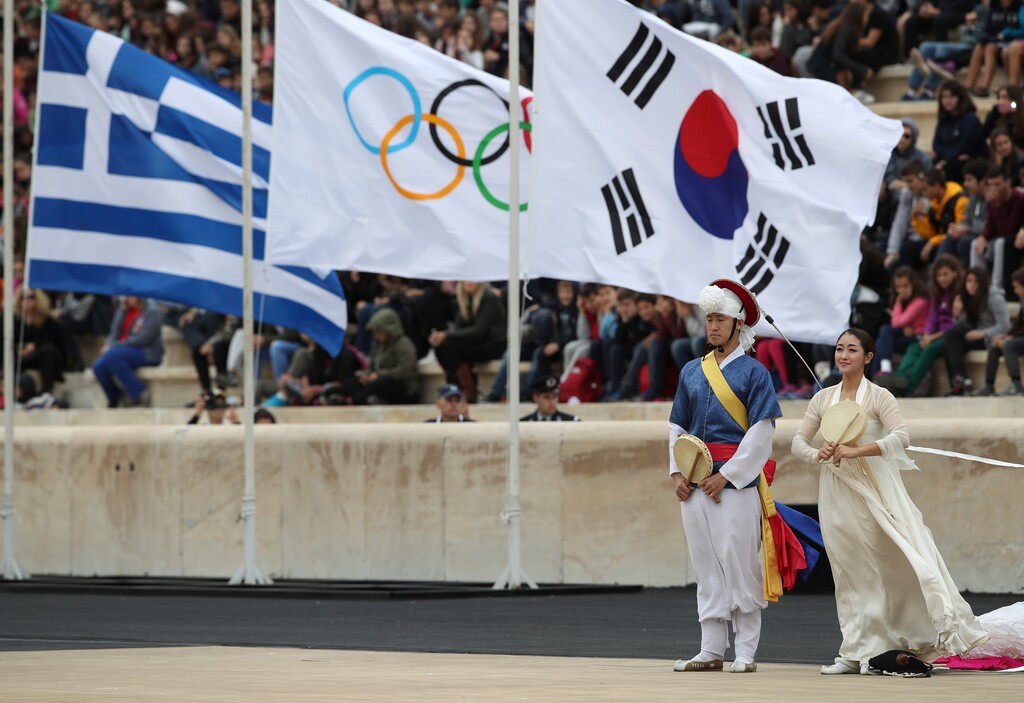 Dancers dressed in traditional costume stand near the Greek, Olympic and South Korean flags during a handover ceremony for the Olympic Flame at Panathenaic stadium in Athens, on Tuesday, Oct. 31, 2017. The South Korean leg of the relay will involve 7,500 torch-bearers, who will cover a total 2,018 kilometers (about 1260 miles) before the opening ceremony in Pyeongchang, which will host the Feb. 9-25, 2018 Winter Olympics. (AP Photo/Petros Giannakouris)