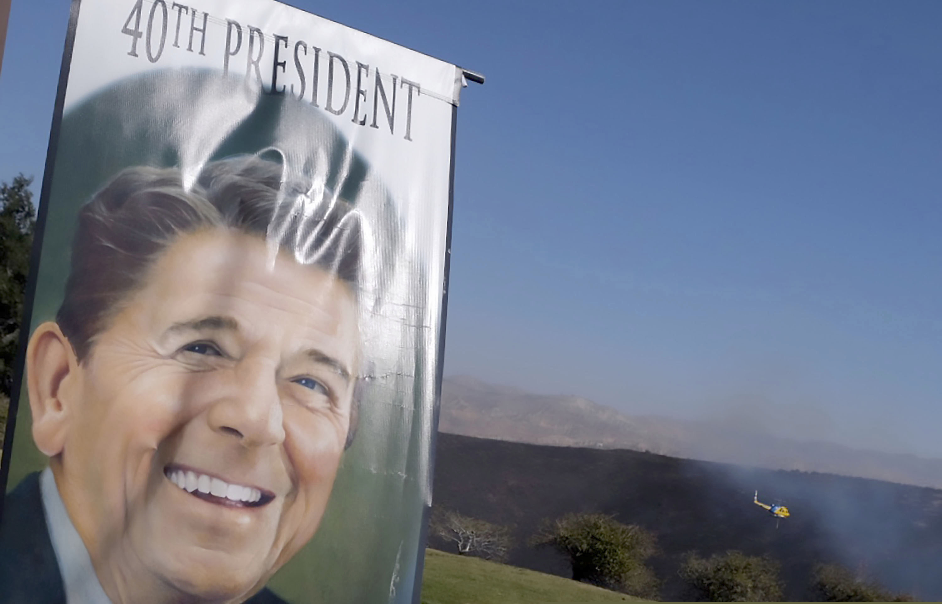 (Dean Musgrove | The Orange County Register/SCNG via AP, file)  A banner hangs at the entrance to the Ronald Reagan Presidential Library as as a helicopter flies over the burned hills on Wednesday, Oct. 30, 2019.