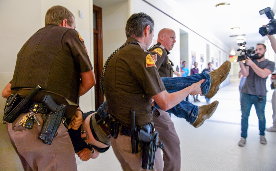 (Leah Hogsten  |  The Salt Lake Tribune) Ethan PetersenÊwithÊCivil Riot, a SLC-basedÊcivilÊresistance collective, and other opponents of the proposed inland port are escorted out of the Utah Inland Port Authority Board meeting by Utah Highway Patrol officers at the Capitol, June 5, 2019. The Inland Port Authority Board had to cancel its meeting last month after a group of protesters took over the meeting. Petersen was arrested.