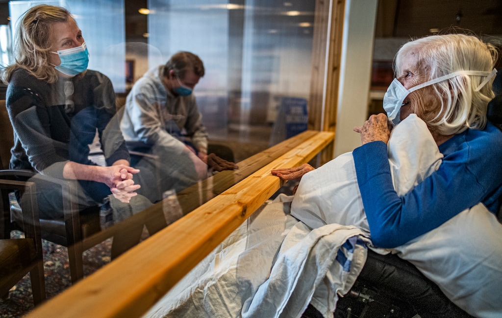 (Richard Tsong-Taatarii | Star Tribune via AP) Carla Gillespie with her son Dylan visited her mother, Evelyn Solberg, at the Jones-Harrison Residence in Minneapolis, Monday, Oct. 12, 2020. It was the first time families have been allowed to visit residents inside nursing homes while masked up and behind a plastic shield since March.