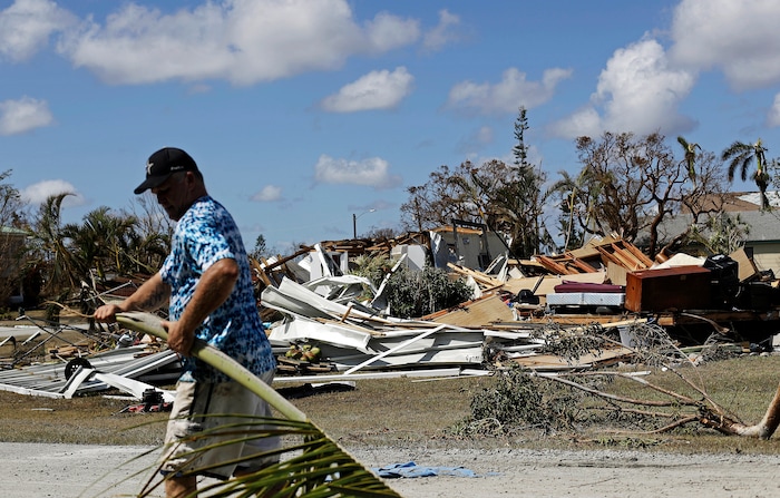 Rob Brehm cleans up debris from his home as a demolished house sits across the street after Hurricane Irma in Goodland, Fla., Tuesday, Sept. 12, 2017. (AP Photo/David Goldman)