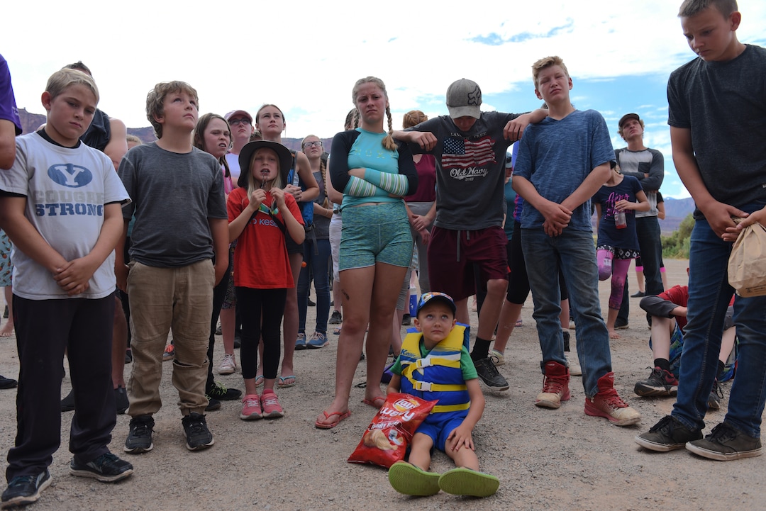 (Shannon Mullane for High Country News) Rally-goers look up at Enoch Foster, who is standing on top of a trailer, as he goes over rafting safety and logistics before leading a prayer near Moab, Utah, on July 27.