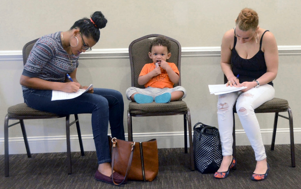 FILE- In this May 15, 2018, file photo, Joan Herrera, center, sits and waits as his mother Andrea Batista Garcia, left, and Marlene Gonzales, fill out job applications while attending the Great Northeast 2018 Job Fair at Capriotti's in McAdoo, near Hazleton, Pa. The U.S. government issues the May jobs report on Friday, June 1. (Ellen F. O'Connell/Hazelton Standard-Speaker via AP, File)