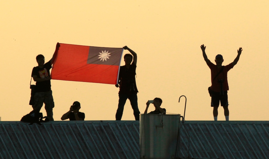 (Wally Santana | AP file photo) Locals on a warehouse rooftop display the national flag while watching Taiwan fighter jets practice during military exercises in Chiayi, central Taiwan in 2014. The Pacific island nation of Kiribati severed ties with Taiwan on Friday, Sept. 20. 2019, the second such loss for diplomatically isolated Taiwan in less than a week.