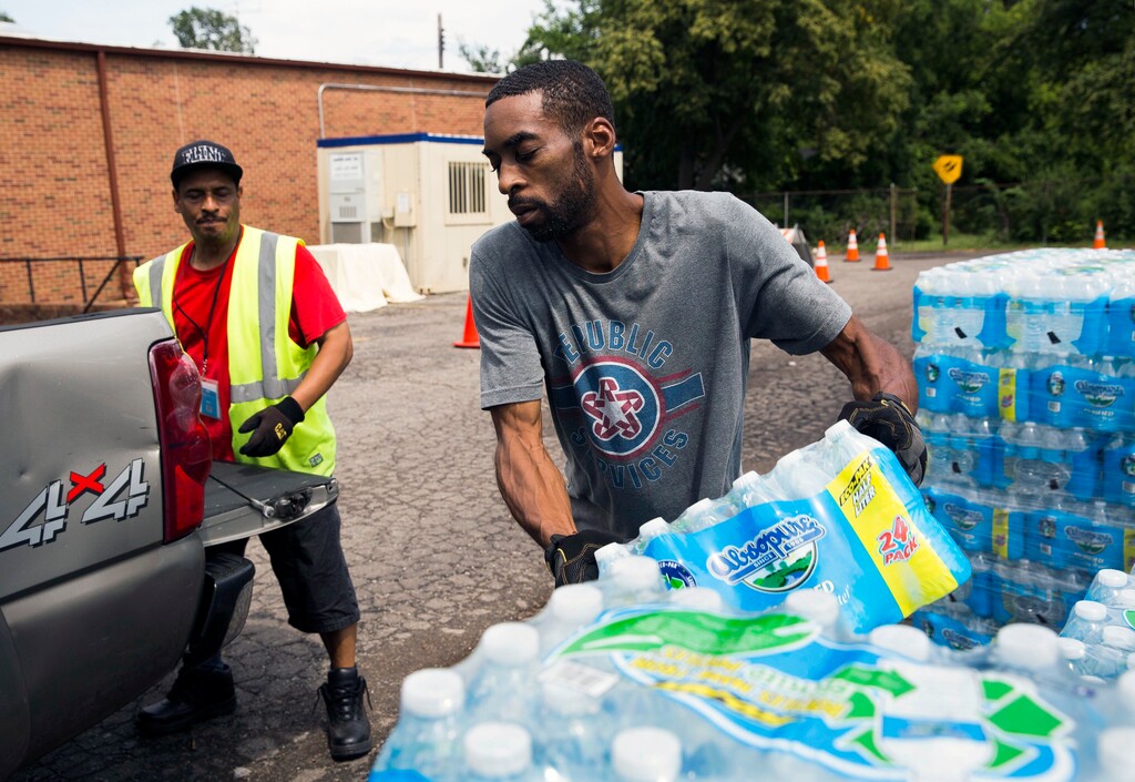In this photo taken Aug. 11, 2017, Shawn Jones, 42, right, and Tony Price, 54, distribute bottled water at a point of distribution in Flint, Mich. Michigan will close the last four locations where Flint, Mich., residents have been getting free bottled water, filters, replacement cartridges and testing kits because the city's water quality has been below federal action levels for lead for nearly two years. (Terray Sylveste /The Flint Journal-MLive.com via AP)