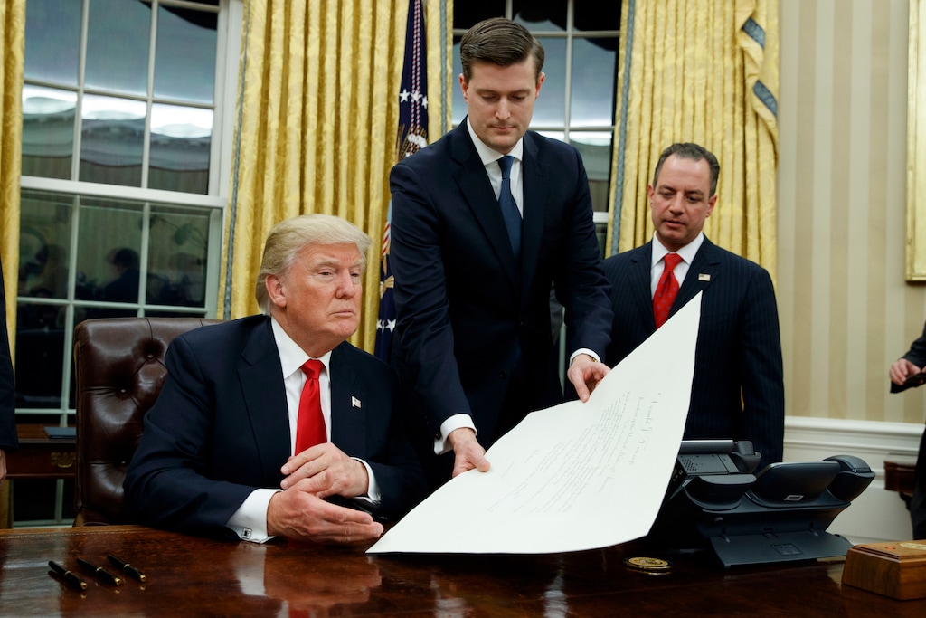 FILE - In this Jan. 20, 2017 file photo, White House Staff Secretary Rob Porter, center, hands President Donald Trump a confirmation order for James Mattis as defense secretary, in the Oval Office of the White House in Washington, as White House Chief of Staff Reince Priebus, right, watches.  Porter is stepping down following allegations of domestic abuse by his two ex-wives.   (AP Photo/Evan Vucci)