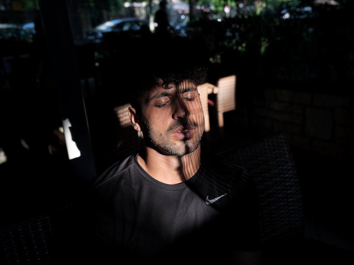 (Myrto Papadopoulos | The New York Times) Hasib Hotak, a homeless refugee from Afghanistan, cools off by a fan outside a kebab restaurant in Athens, Greece, July 25, 2020. Around the world, the poor and marginalized are much more likely to be vulnerable to extreme heat; Hasib sleeps with other refugees on a rooftop that turns blazing hot by midday.