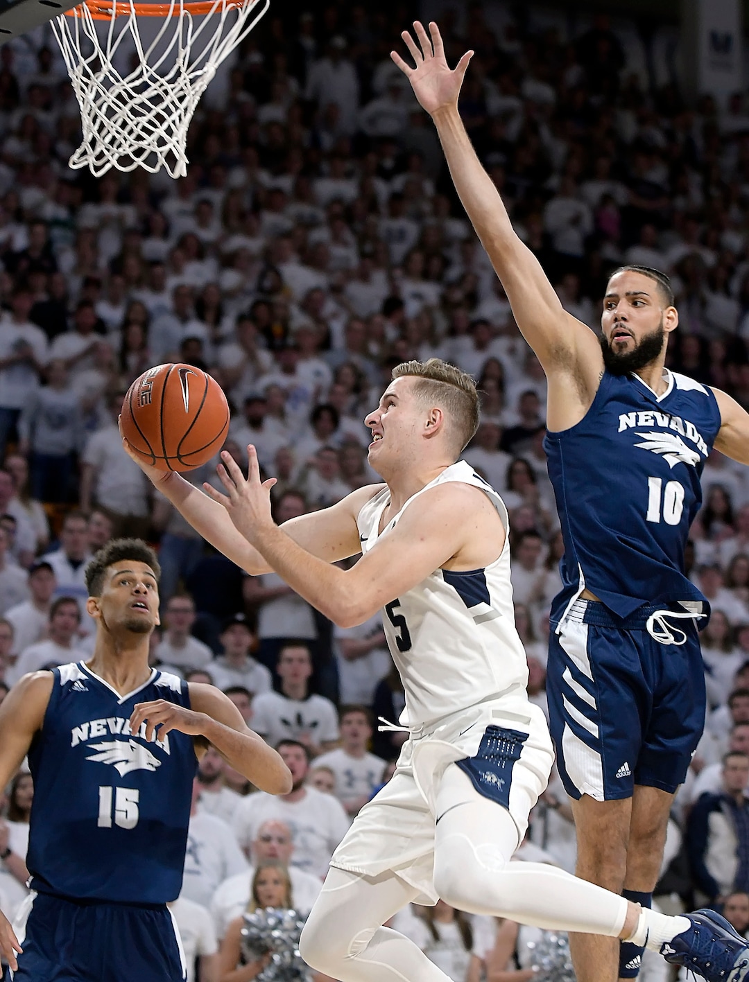 (Eli Lucero  |  The Herald Journal via AP) Utah State guard Sam Merrill (5) drives to the basket as Nevada forward Trey Porter (15) and forward Caleb Martin (10) defend during an NCAA college basketball game, Saturday, March 2, 2019, in Logan, Utah.