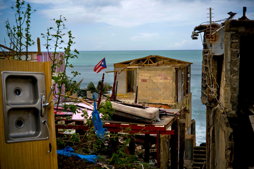 (AP Photo/Ramon Espinosa) In this Oct. 5, 2017 file photo, a Puerto Rican national flag is mounted on debris of a damaged home in the aftermath of Hurricane Maria in the seaside slum La Perla, San Juan, Puerto Rico. An independent investigation ordered by Puerto Rico’s government estimates that nearly 3,000 people died as a result of Hurricane Maria. The findings issued Tuesday, Aug. 28, 2018, by the Milken Institute School of Public Health at George Washington University contrast sharply with the official death toll of 64.