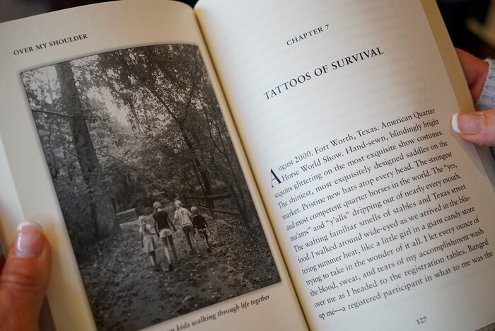 In this Wednesday, March 27, 2019, photo, Kacey Ruegsegger Johnson looks at a photo of her children in a galley copy of her new memoir at her home in Cary, N.C. For the last 20 years since she was injured in the Columbine High School attack, she has lived with post-traumatic stress disorder, along with physical pain. (AP Photo/Allen G. Breed)