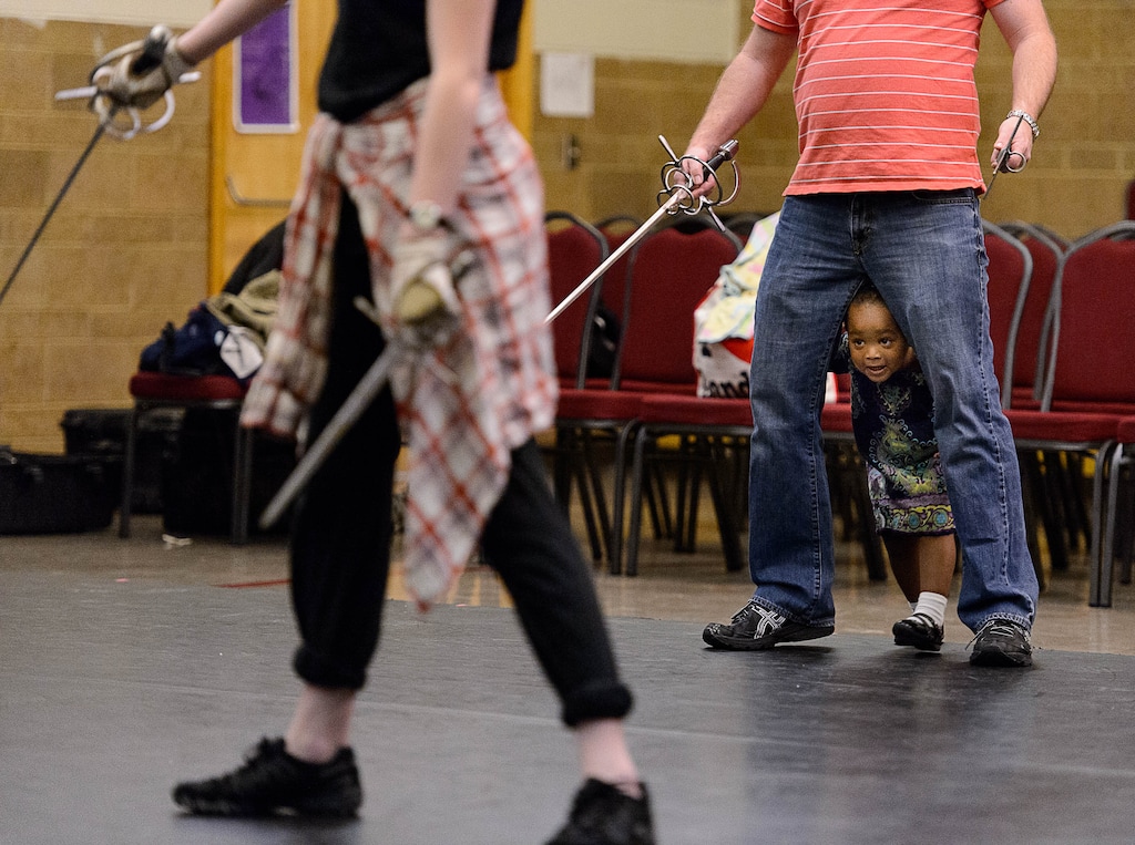 Trent Nelson | The Salt Lake Tribune
With his daughter, London, between his legs, Jared Larkin teaches a stage combat class at Salt Lake School for the Performing Arts, Tuesday, June 2, 2015. Working on a fight routine are students Gerard Black and Hana Neves.