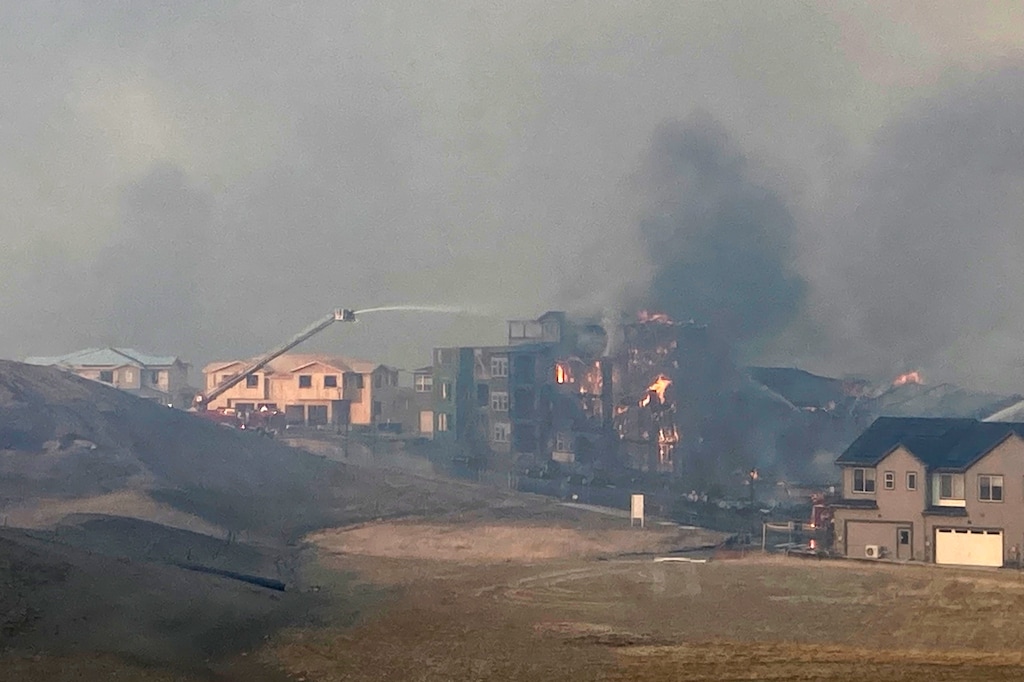 (AP Photo | David Zelio) Firefighters spray water on a structure fire as a wildfire burns, Thursday, Dec. 30, 2021, in Superior, Colo. Thousands of residents in Superior and Louisville, two communities near Denver, were ordered to evacuate Thursday because of a wind-fueled wildfire that engulfed parts of the area in smoky, orangish skies.