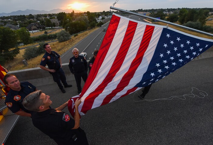 (Francisco Kjolseth  |  The Salt Lake Tribune)  Firefighters unfurl a flag as they get ready to honor Utah firefighter Matt Burchett, 42, who died fighting a wildfire in California. His body was being returned home, to travel along I-215 after being flown in to the Utah Air National Guard in Salt Lake City on Wed. Aug. 15, 2018. The remains of the Draper battalion chief were transported to Jenkins-Soffe Mortuary in South Jordan.