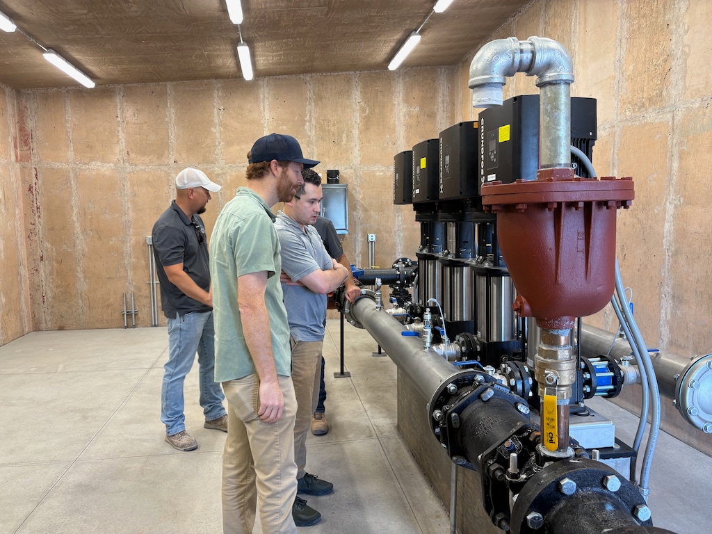 Men stand in front of a system of pipes in a cement structure.