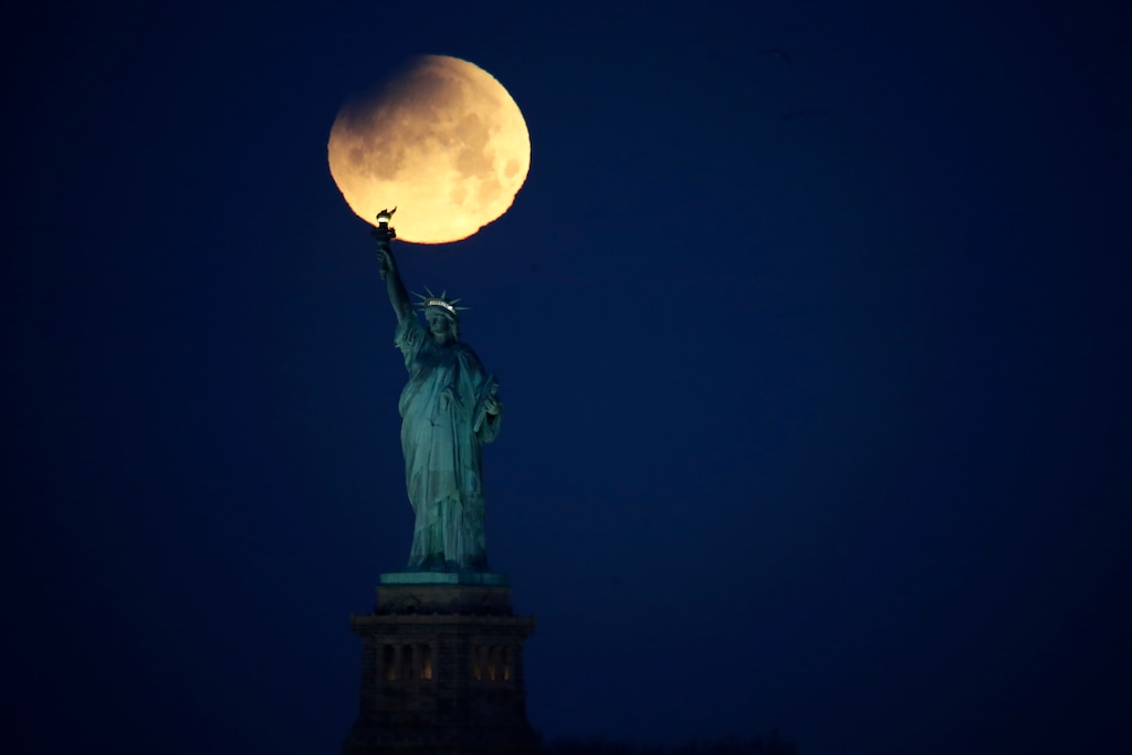 The Statue of Liberty is backdropped by a supermoon, Wednesday, Jan. 31, 2018, seen from the Brooklyn borough of New York. The supermoon, which is the final of three consecutive supermoons, also experience lunar eclipse as it set over the horizon, but only a partial eclipse was visible in the East Coast. (AP Photo/Julio Cortez)