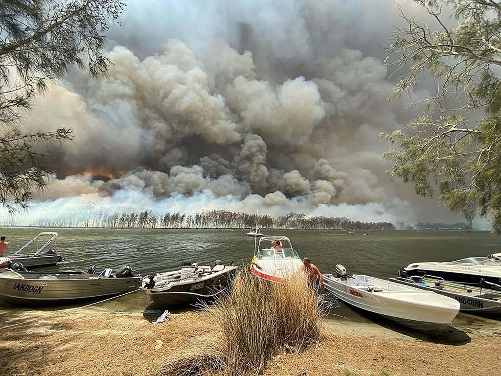(Robert Oerlemans via AP) Boats are pulled ashore as smoke and wildfires rage behind Lake Conjola, Australia, Thursday, Jan. 2, 2020. Thousands of tourists fled Australia's wildfire-ravaged eastern coast Thursday ahead of worsening conditions as the military started to evacuate people trapped on the shore further south.