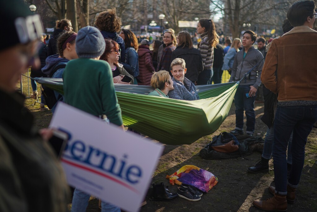 (Chang W. Lee | The New York Times)
Hayley Smith, left, and Avery Fessenden hang out in a hammock amidst people gathered before Sen. Bernie Sanders (I-Vt.) spoke on the University of Michigan campus in Ann Arbor, Mich., March 8, 2020. "It's the job of the activist left to push political limits, staking out positions that sound radical today but could, with enough work, seem like common sense in the future," writes The New York Times columnist Michelle Goldberg.