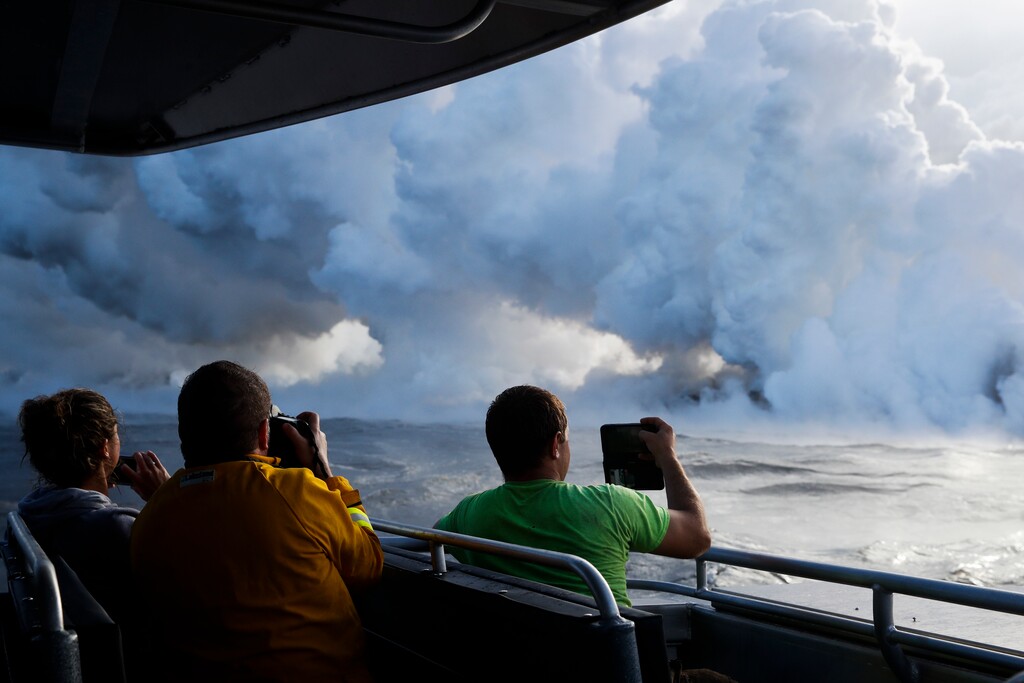 People take pictures as lava enters the ocean, generating plumes of steam near Pahoa, Hawaii Sunday, May 20, 2018. Kilauea volcano that is oozing, spewing and exploding on Hawaii's Big Island has gotten more hazardous in recent days, with rivers of molten rock pouring into the ocean Sunday and flying lava causing the first major injury. (AP Photo/Jae C. Hong)