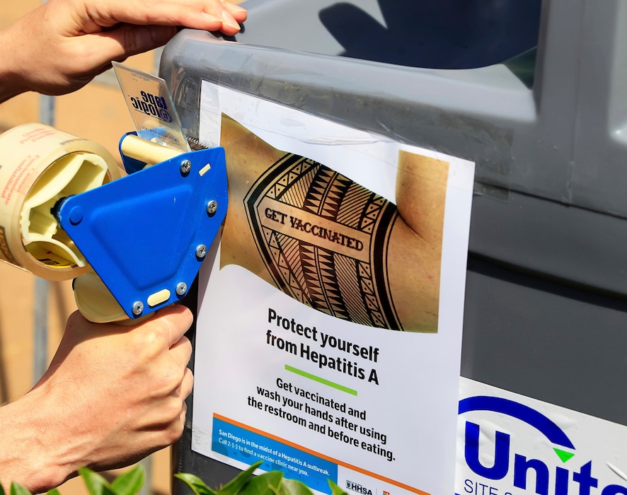 (Eduardo Contreras | The San Diego Union-Tribune | The Associated Press) In this Friday, Sept. 1, 2017, file photo, a worker tapes signage telling people to get vaccinated to protect themselves against Hepatitis A, onto sinks installed at the Neil Good Day Center on 17th Street downtown in San Diego. A San Diego County grand jury report faults local response to a recent hepatitis A epidemic and recommends improving lines of communication to prepare for future health emergencies. The San Diego Union-Tribune newspaper says the 20-page report released Thursday, May 17, 2018, commends officials for effectively contacting at-risk residents and getting them vaccinations.