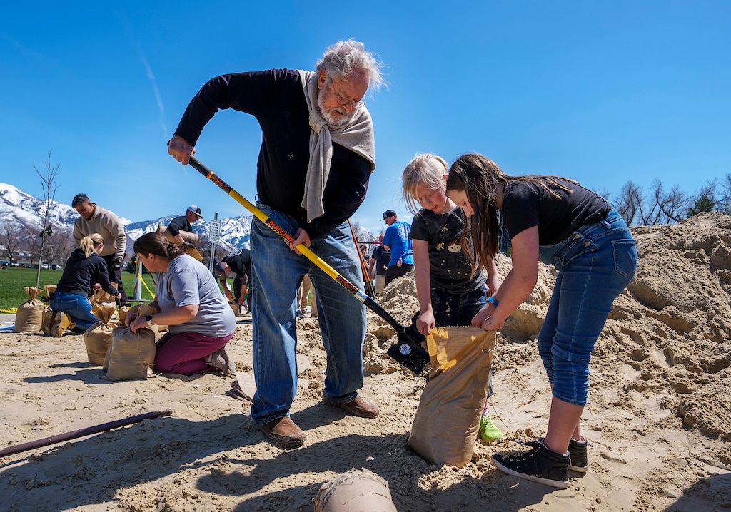 (Leah Hogsten | The Salt Lake Tribune) Pat Shea, left, and his goddaughters Inara Bennett and Katie Bennett join hundreds of fellow volunteers to fill sandbags at Sugar House Park, April 15, 2023 to mitigate flooding in Salt Lake City. Volunteers were able to take home 10 sandbags for their effort.
