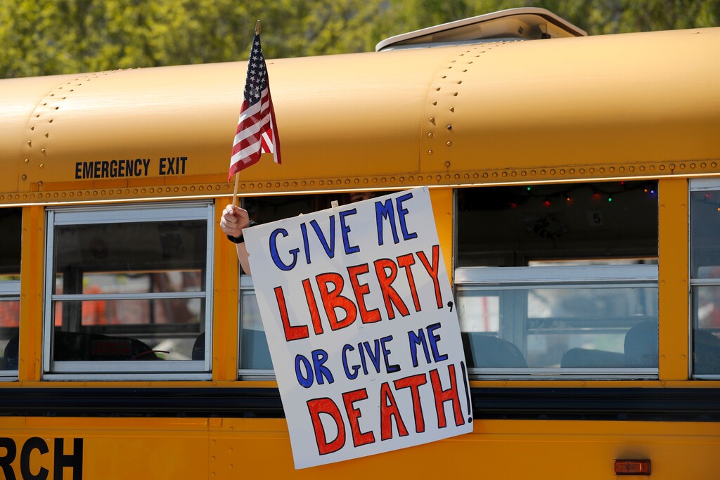 A person holds a sign while waving a flag in the direction of people gathered voice their opposition to stay-at-home orders put into place due to the COVID-19 outbreak outside the Missouri Capitol Tuesday, April 21, 2020, in Jefferson City, Mo. Several hundred people gathered to protest the restrictions and urge a restart to the economy shutdown due to the coronavirus. (AP Photo/Jeff Roberson)