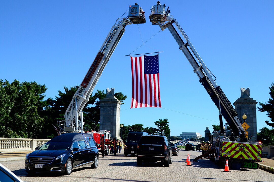(Danny La | Special to The Tribune) The United States flag is displayed near the entrance of Arlington National Cemetery by Arlington and Alexandria Fire Department firefighters as they salute during the funeral procession for Staff Sgt. Taylor Hoover proceeds on Friday, Sept. 24, 2021. Hoover was killed in action due to a suicide bombing in Kabul, Afghanistan on Aug. 26.
