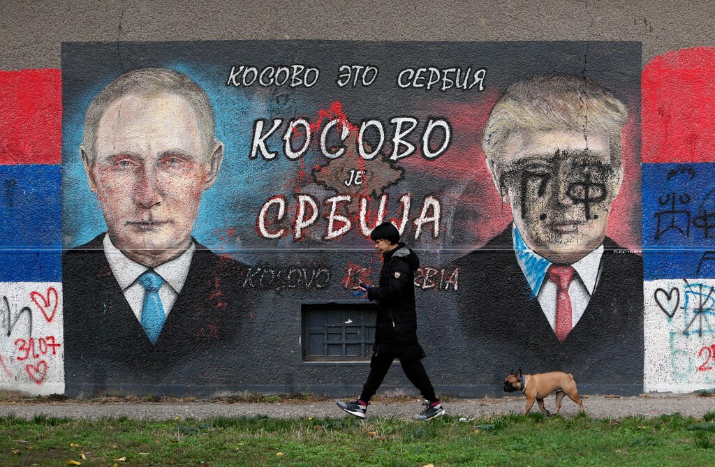 A woman with a dog passes by graffiti depicting the Russian President Vladimir Putin, left, and U.S. President Donald Trump vandalized with paint in a suburb of Belgrade, Serbia, Tuesday, Nov. 3, 2020. (AP Photo/Darko Vojinovic)