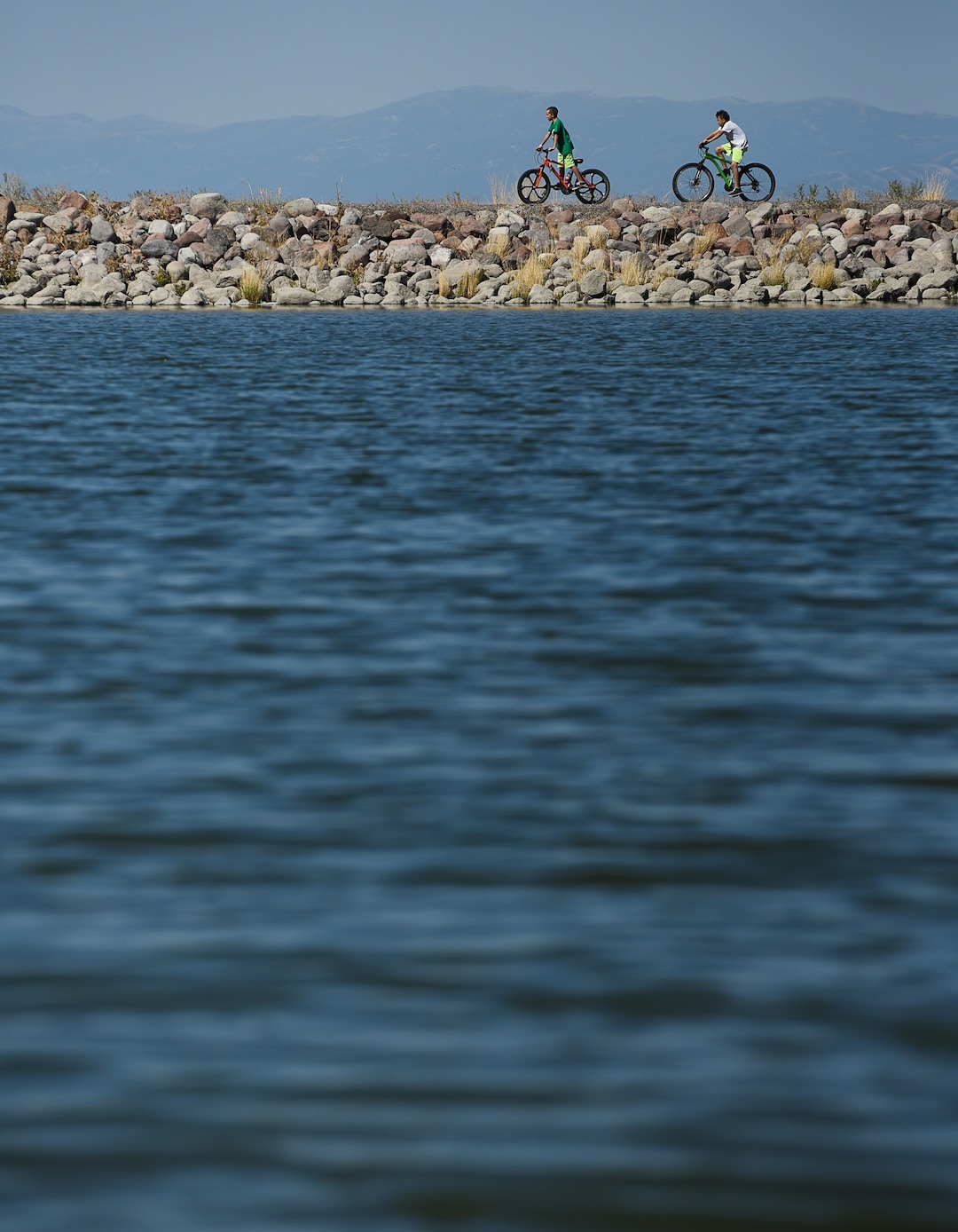 (Francisco Kjolseth  |  The Salt Lake Tribune)  Kids ride their bikes around the popular Black Ridge Reservoir in Herriman on Tuesday, Aug. 28, 2018, where warning signs have been posted after an outbreak of algae-related toxin cyanobacteria was detected in the water.