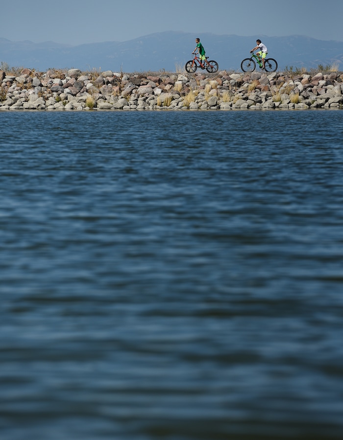 (Francisco Kjolseth  |  The Salt Lake Tribune)  Kids ride their bikes around the popular Black Ridge Reservoir in Herriman on Tuesday, Aug. 28, 2018, where warning signs have been posted after an outbreak of algae-related toxin cyanobacteria was detected in the water.