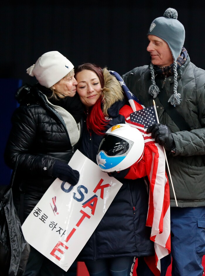Katie Uhlaender of United States, center, is hugged and kissed by Jean Schaefer, left, and Dr. Brian Boxer Wachler in the finish area after the final run of the women's skeleton competition at the 2018 Winter Olympics in Pyeongchang, South Korea, Saturday, Feb. 17, 2018. Schaefer is the mother of deceased American bobsledder Steve Holcomb and Wachler is a Holcomb family friend and doctor. They came to support Uhlaender, who was friends with Holcomb. (AP Photo/Andy Wong)