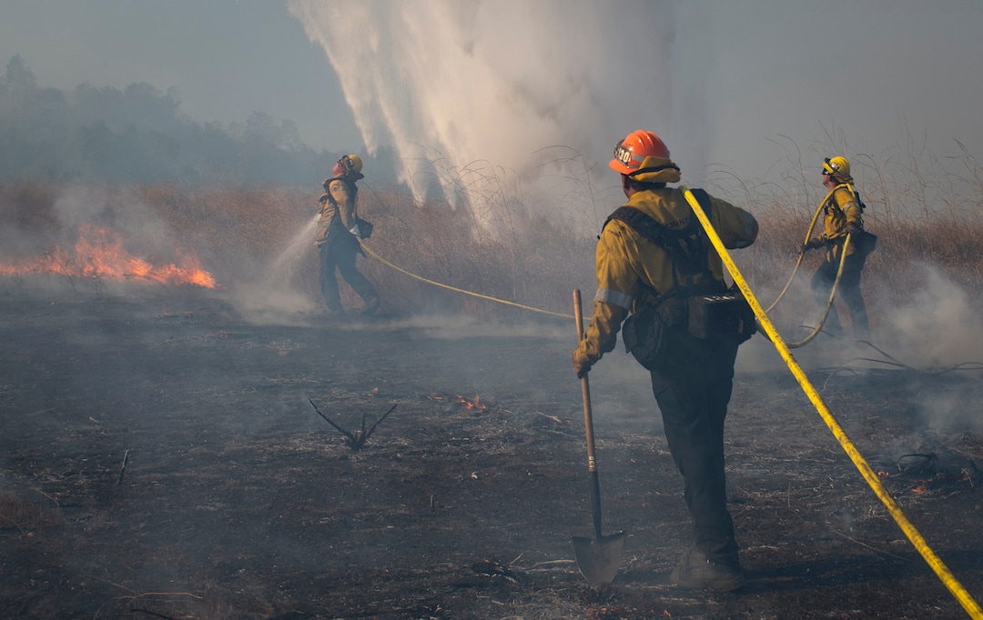 (Christian Monterrosa | AP)  Firefighters work to prevent flames from reaching nearby homes as a helicopter drops water during the Easy Fire, Wednesday, Oct. 30, 2019, in Simi Valley, Calif.