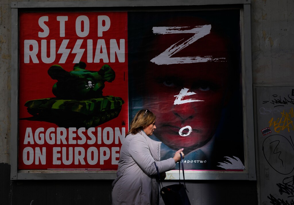 (Petr David Josek | AP) A woman walks past a wall with posters depicting Russian President Vladimir Putin, right, in Warsaw, Poland, on Thursday, March 24, 2022.