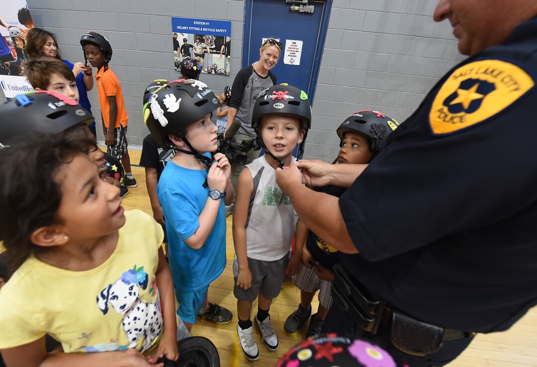 (Francisco Kjolseth  |  The Salt Lake Tribune)  Detective Greg Wilking helps kids set up their new helmets. In advance to the upcoming Tour of Utah bicycle race, more than 50 Salt Lake City-area kids received a new bicycle helmet at the Capitol West Boys & Girls Club on Tuesday, July 31, 2018. As part of UnitedHealthcare's Pro Cycling team and community outreach program to keep kids healthy and active, team cyclists Jonny Clarke and Sebastian Haedo engage the kids in a few warm up routines before getting on the bike.