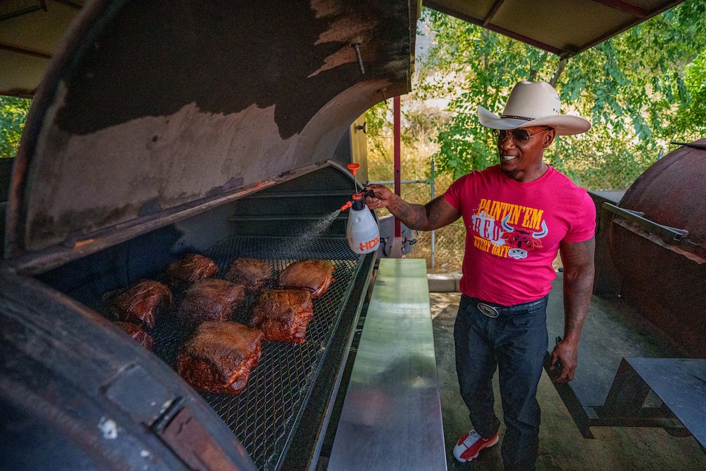(Trent Nelson  |  The Salt Lake Tribune) Les Rhodes Jr., founder of Les BBQ, sprays a solution of apple cider vinegar and water on slabs of meat in Salt Lake City on Tuesday, Aug. 6, 2024.