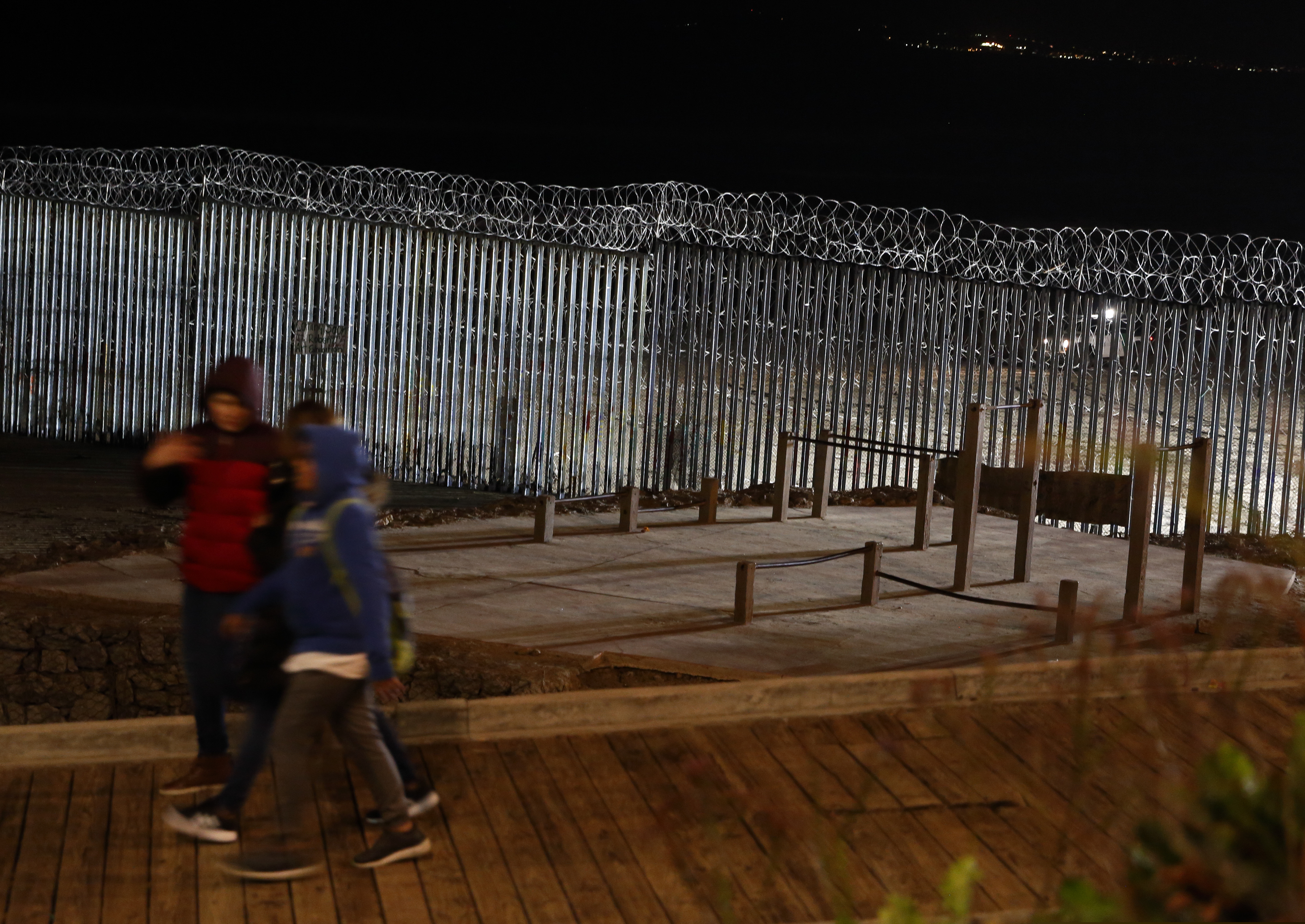 (Gregory Bull | The Associated Press) Floodlights from the U.S. illuminate the border wall, topped with razor wire, as people pass Monday, Jan. 7, 2019, at the beach in Tijuana, Mexico. With no breakthrough in sight, President Donald Trump argued his case to the nation Tuesday night that a "crisis" at the U.S.-Mexico border requires the long and invulnerable wall he's demanding before ending the partial government shutdown.