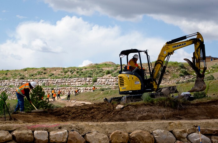 In a Wednesday, May 8, 2019 photo, workers from Hadco Construction aid the efforts of volunteers as they all help to complete an Eagle Scout Service Project that aims to create a walkable path connecting nearby neighborhoods to Ignite Entrepreneurship Academy and a future park just northwest of the charter school in Lehi, Utah. (Isaac Hale/The Daily Herald via AP)