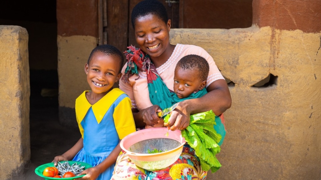 (UNICEF via The Church of Jesus Christ of Latter-day Saints) Happiness, left, sits with her mother, Mary, who carries 1-year-old Laphael while chopping vegetables outside a house in southern Malawi.