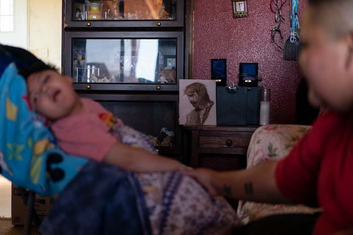 On a small table next to an image of Jesus in a crown of thorns, the ashes of Gloria Uriarte, right and her mother, Eva Dinehdeal, are displayed on a table in Tuba City, Ariz., on April 22, 2020. In the foreground at left is Gloria's son, Curly, as his aunt Christina Dinehdeal holds his hand. The Navajo reservation has some of the highest rates of coronavirus in the country. If Navajos are susceptible to the virus' spread in part because they are so closely knit, that's also how many believe they will beat it. (AP Photo/Carolyn Kaster)